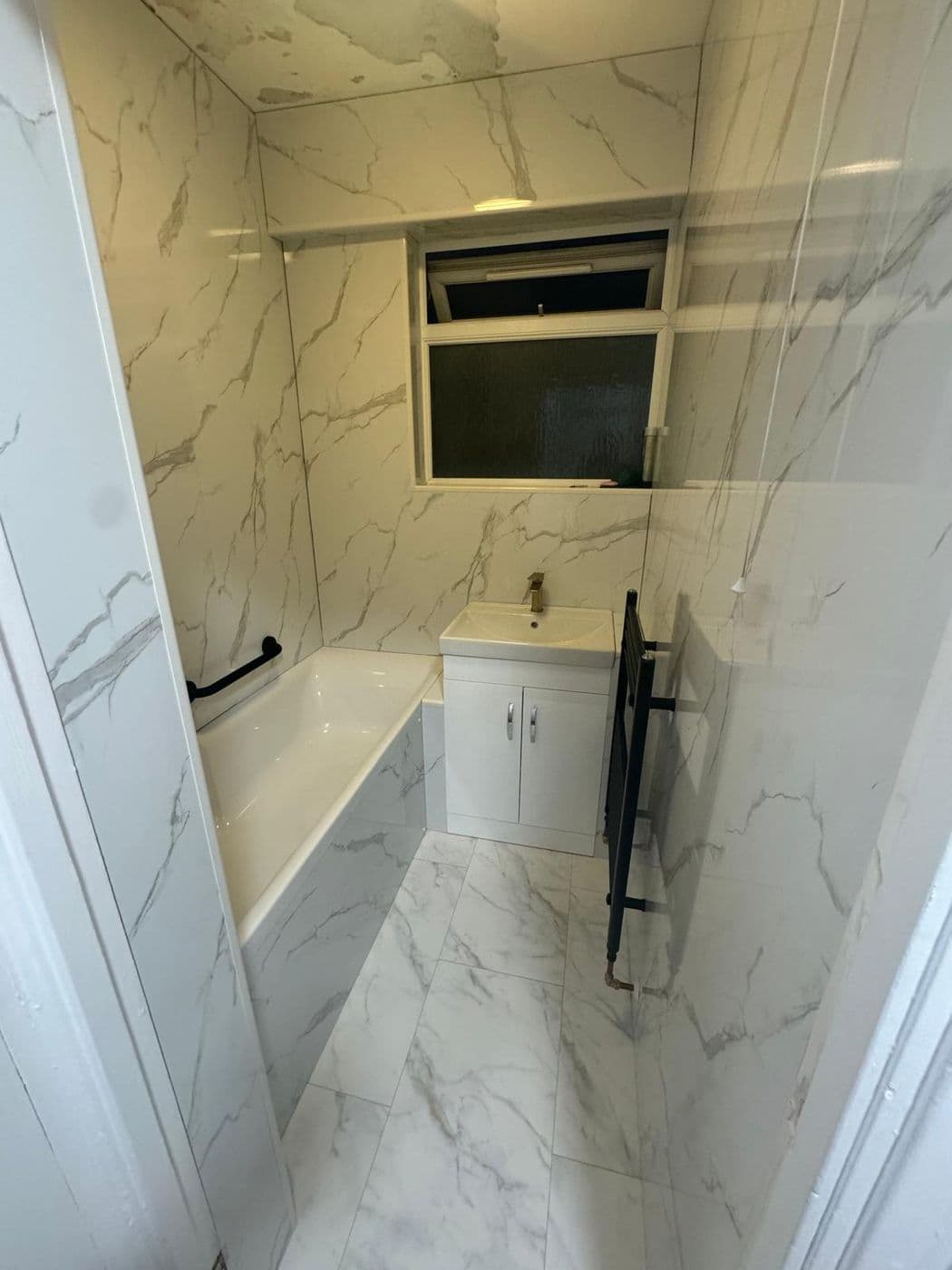 The finished bathroom tiled in large-format marble-effect porcelain with a new bath and vanity unit