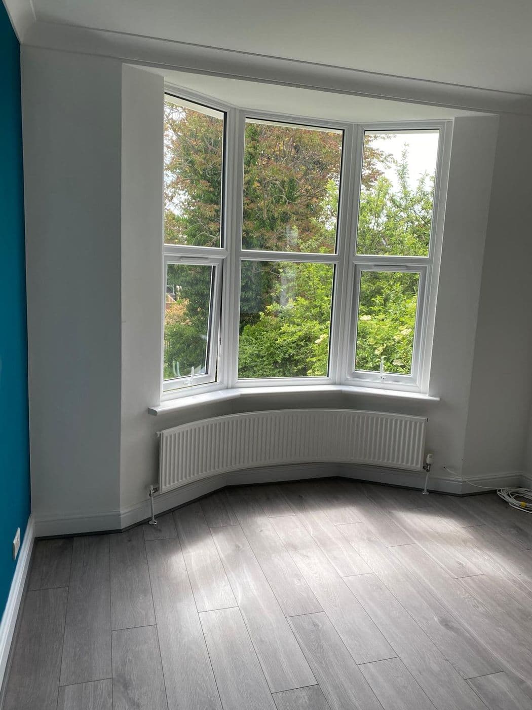 The finished room with a teal feature wall, white bay and grey laminate flooring
