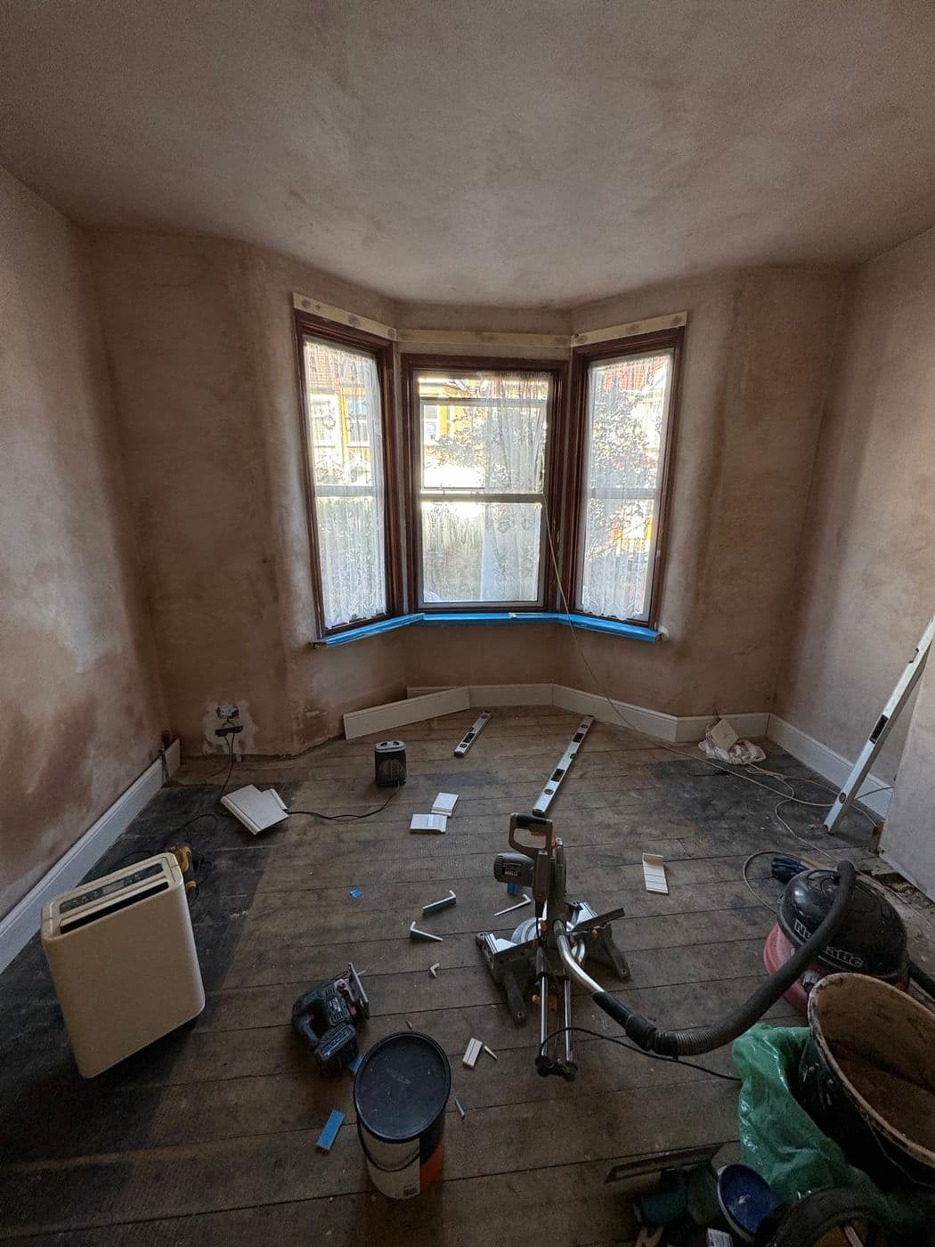 The bay-window room before work, stripped back to bare pink plaster and floorboards