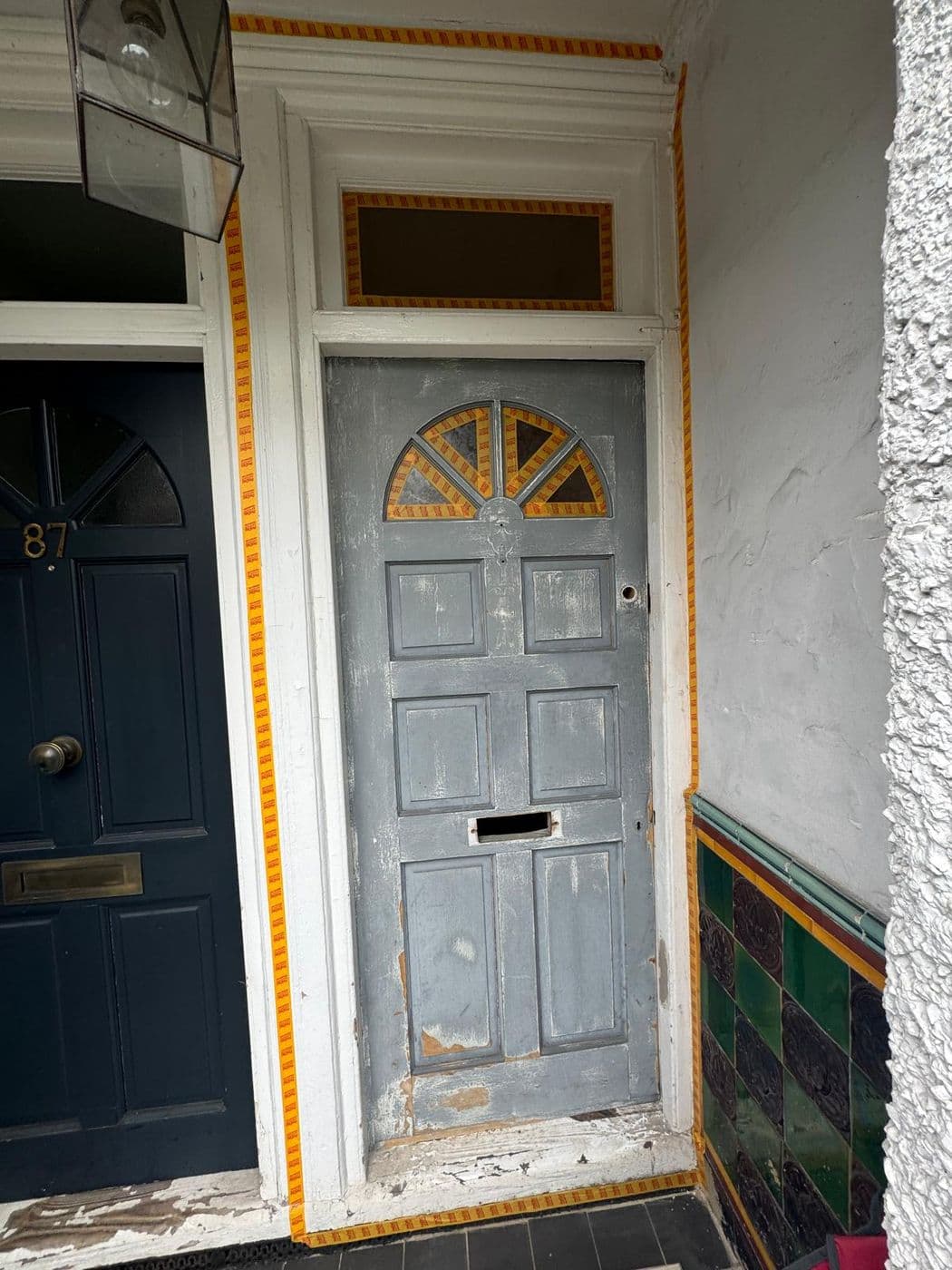 The front door before work, stripped back and primed grey with peeling paint at the base