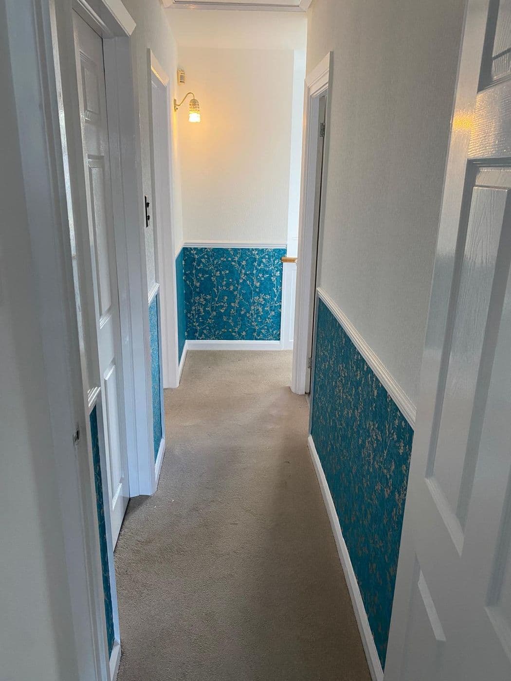 The finished hallway with teal patterned wallpaper below the dado rail and white above