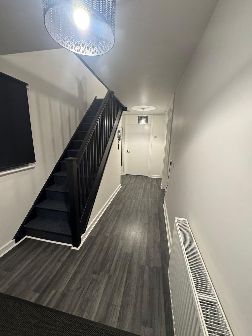 The finished hallway with a black staircase and spindles, white walls and grey wood-effect flooring