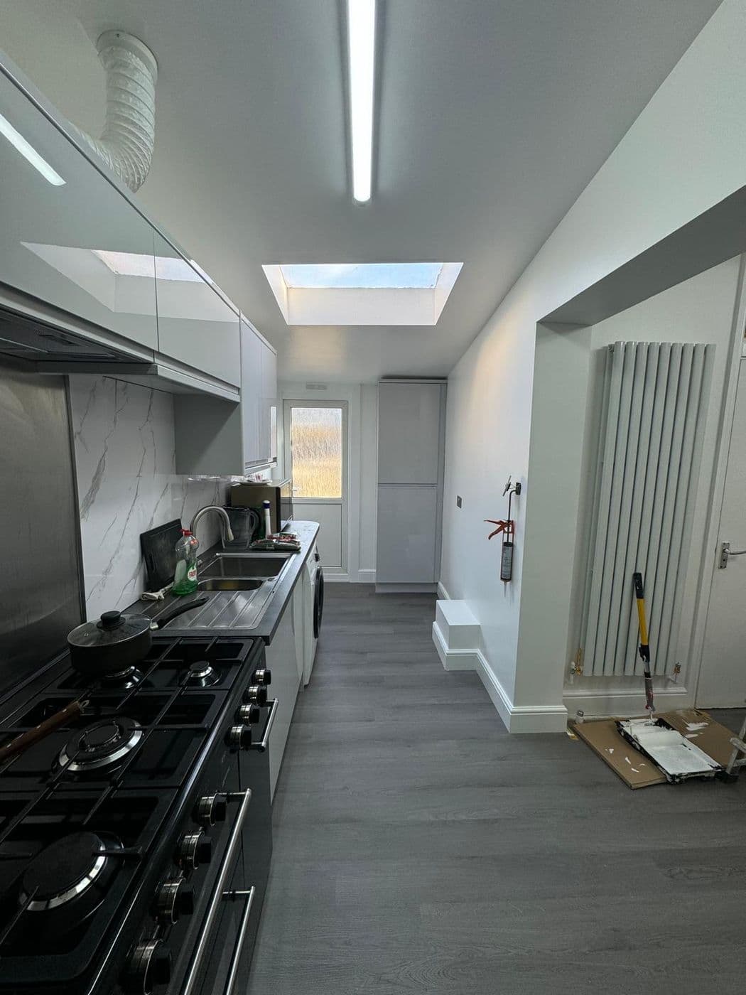Finished galley kitchen with gloss units, a range cooker, marble-effect splashback and a rooflight above